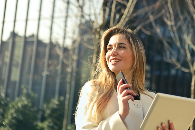 Smiling person with long blonde hair holding a phone up to their ear